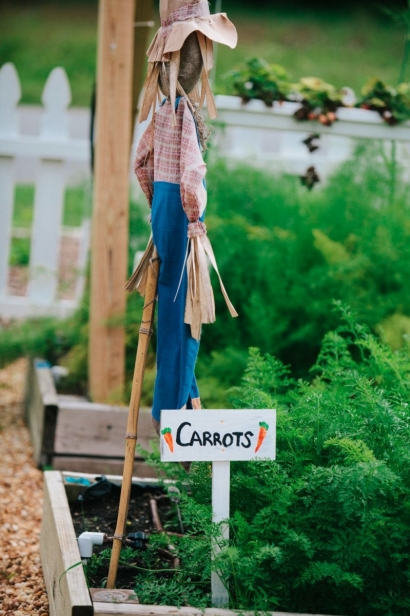 a sign indicating carrots are growing in the garden and a scarecrow at Beam garden in jax beach