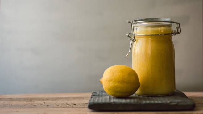 Meyer lemon curd in a jar with a lemon on a wood table