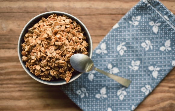 bowl of granola with spoon on wooden table and blue napkin